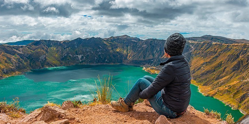 Woman sitting on the edge of the crater lake Quilotoa in Ecuador.