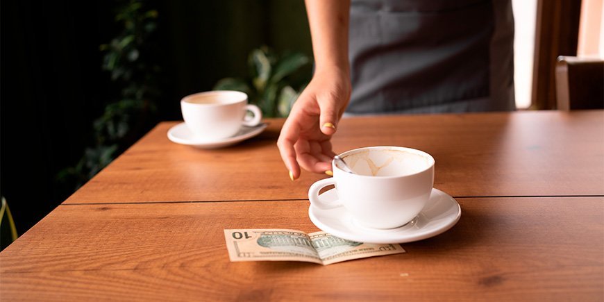 Waiter takes a cup and tip from a table in a cafe