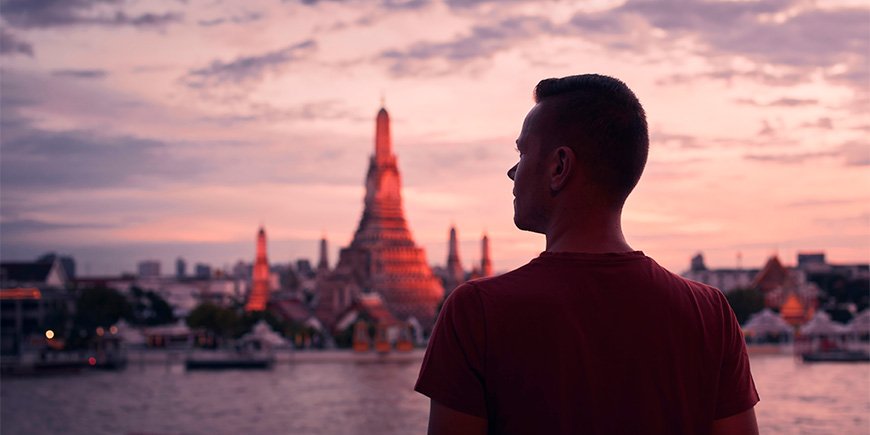 Man standing in front of Wat Arun in Thailand at sunset