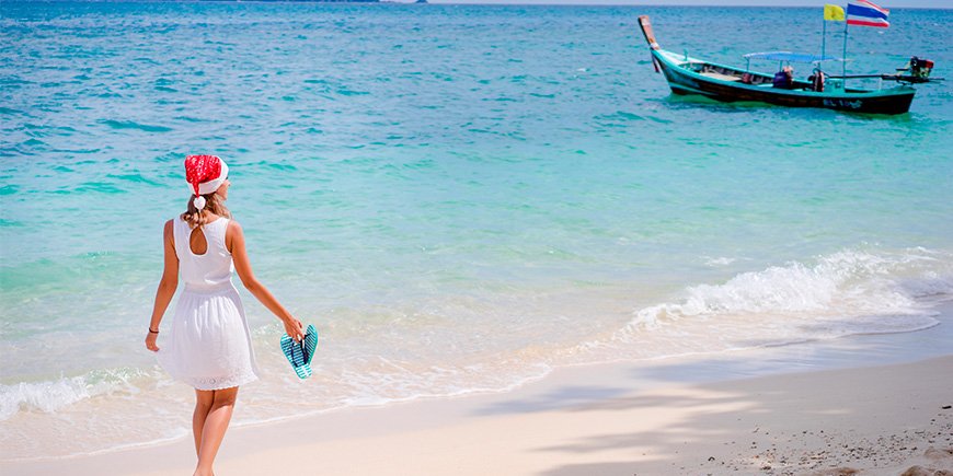 Woman walks on the beach in Thailand wearing a Santa hat