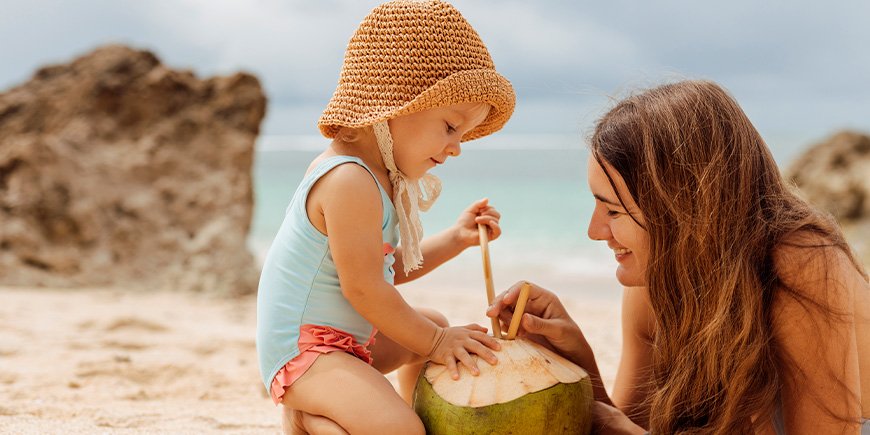 Mum and daughter drinking from a coconut on a beach in Thailand